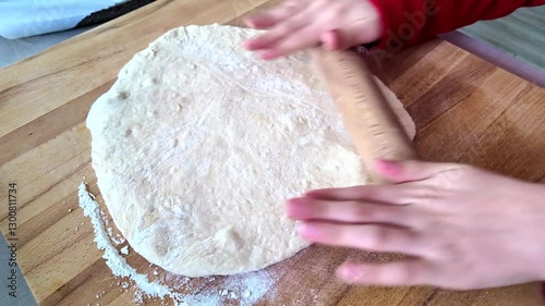 A young child rolls out pizza dough on a floured surface. Only the child's hands and arms are visible; the face is not shown.