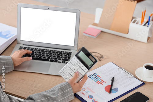 Young businesswoman with laptop and calculator working on report at table in office, closeup