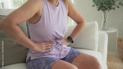 Asia adult middle age woman sit at sofa home feel pain elder gut health care aging system medical issue. Asian female old people Suffer stress cramp abdomen ache cancer illness menses period injury.
