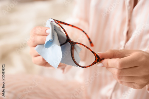 Young woman in pajamas wiping new eyeglasses at home, closeup