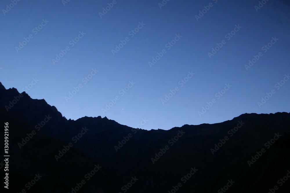 Obraz premium A serene twilight scene over a mountain ridge, with the last light of day fading into the deep blue sky. A single bright star appears in the evening sky, adding a touch of wonder to landscape.