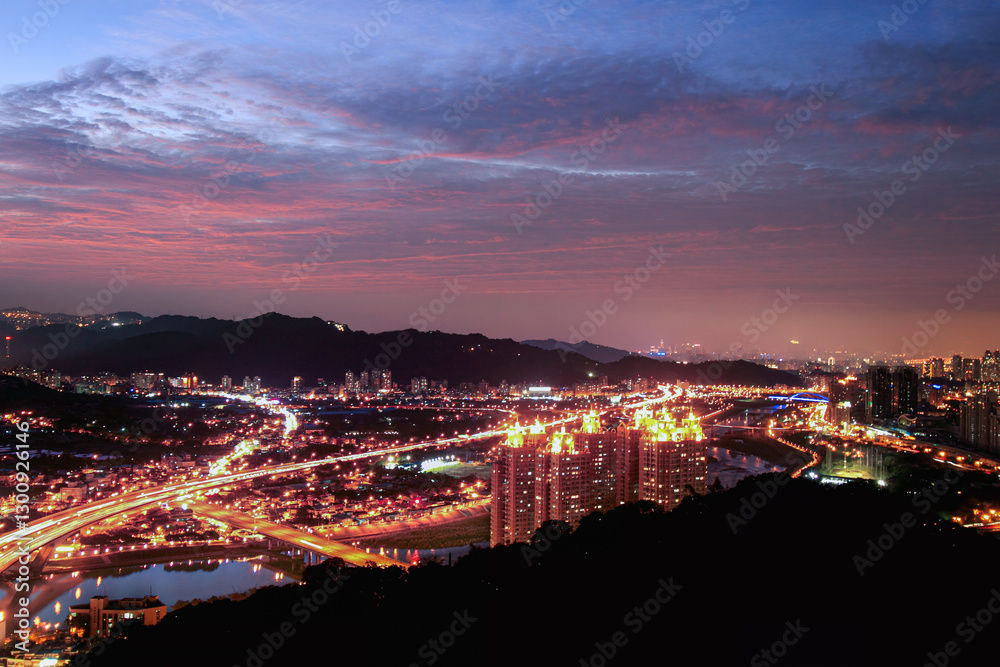 Fototapeta premium A stunning cityscape at dusk featuring brightly lit highways and high-rise buildings. Shizaitou Mountain, New Taipei City, Taiwan.