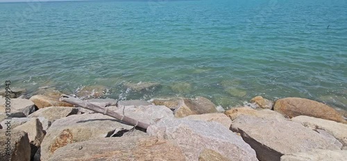 Calm Ocean Waves Gently Lapping Against Rocky Shoreline Under Blue Sky