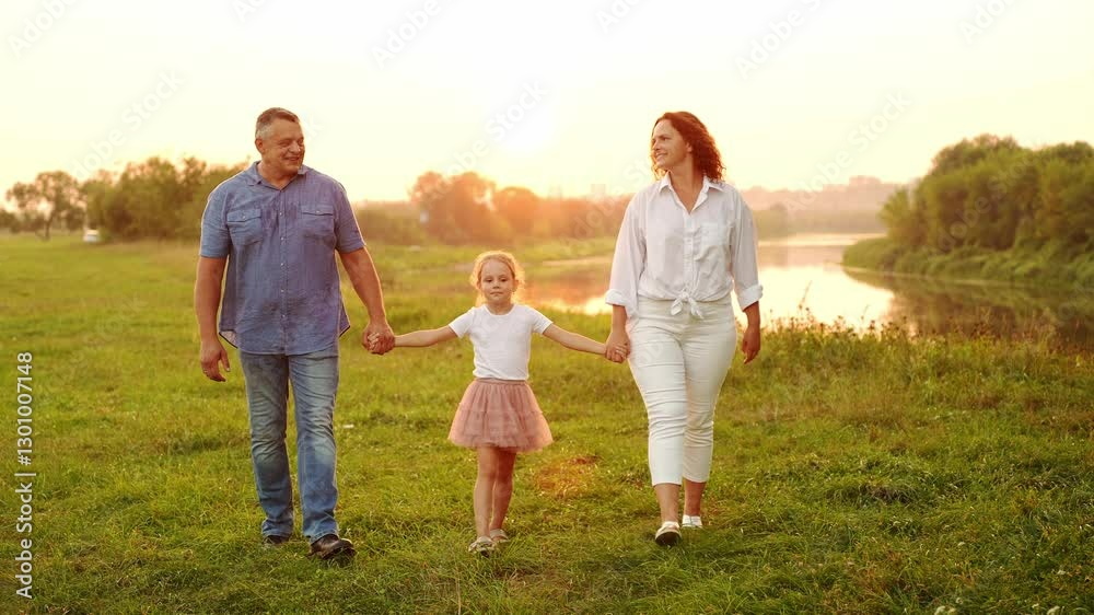 Family spending time together in summer, walking near pond in park at sunset. Mom, dad, girl, walking holding hands, smiling happily, looking at each other. Concept of love and parenthood, childhood Family spending time together in summer, walking near pond in park at sunset. Mom, dad, girl, walking holding hands, smiling happily, looking at each other. Concept of love and parenthood, childhood