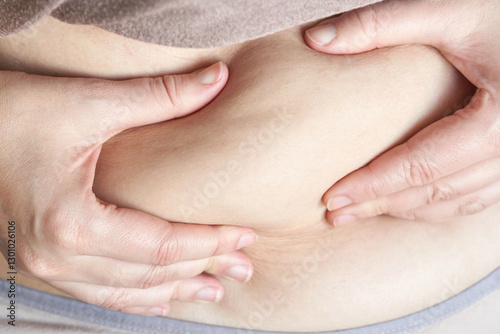 Close up of female hands pinching belly skin highlighting body awareness and health focus. photo