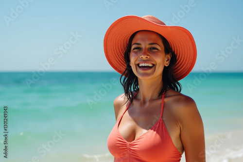 A joyful woman with wet, dark hair wearing a bright orange hat and matching bikini, standing on a sunny beach with light tanned skin.