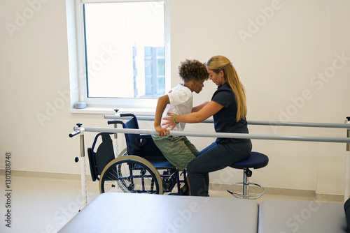 Quadro em tela Female physiotherapist helps young patient practice standing up from wheelchair