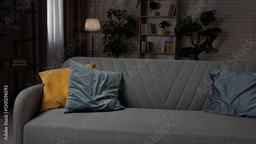 Close shot of living room in cozy apartment, modern sofa standing in the middle of the room with colorful pillows, low light and modern furniture creating stylish atmosphere.