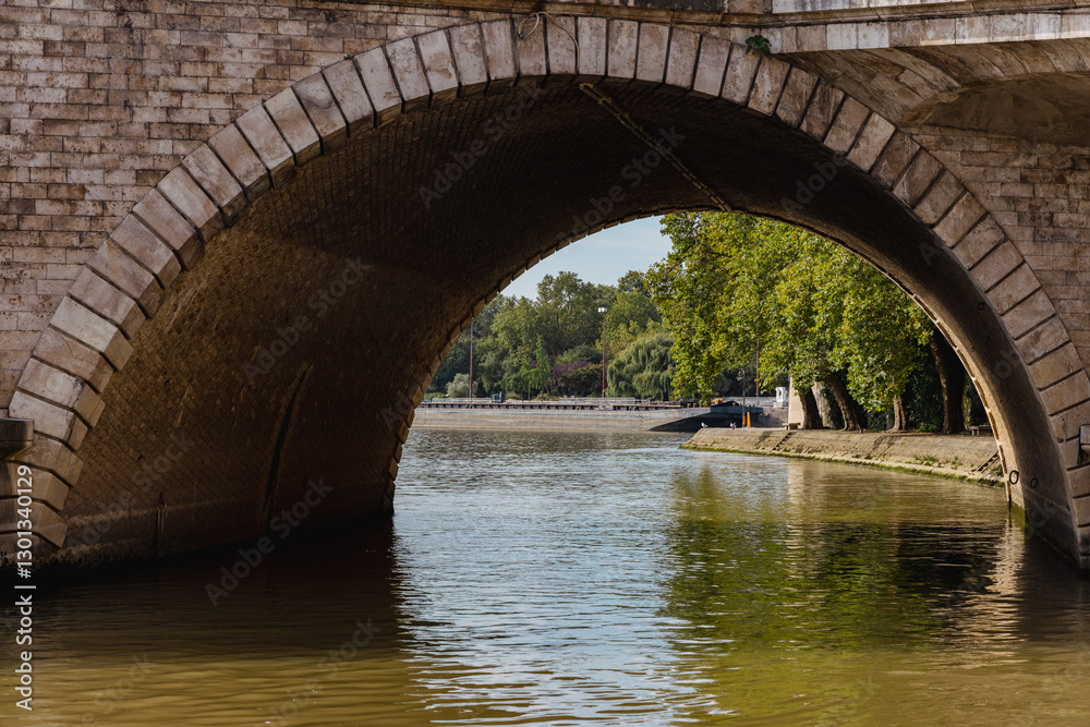 View of seine river in paris, lookiing through the arch of a road bridge made of stone bricks. sunny day, green water