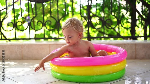 Little girl sits in an inflatable pool on the balcony and reaches for flying soap bubbles. High quality 4k footage