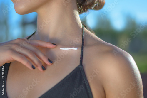 Aesthetic portrait of a dark-haired girl applying sunscreen on her body under the sun. Skin protection from UV rays.