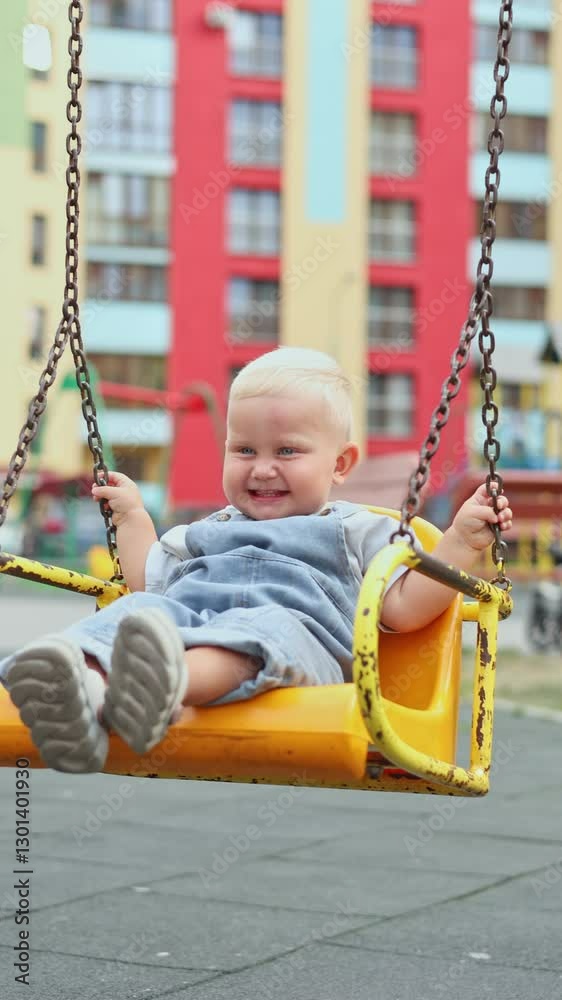 Toddler boy playing on playground in summer under the sun. Child playing in kindergarten yard. Active child on colorful swing. Healthy summer activity for kids. Little boy swinging. Toddler boy playing on playground in summer under the sun. Child playing in kindergarten yard. Active child on colorful swing. Healthy summer activity for kids. Little boy swinging.
