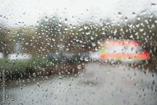 Abstraktes Motiv mit Regentropfenmuster auf Glasscheibe vor Krankenwagen auf Krankenhausparklatz bei Regen am Morgen im Winter