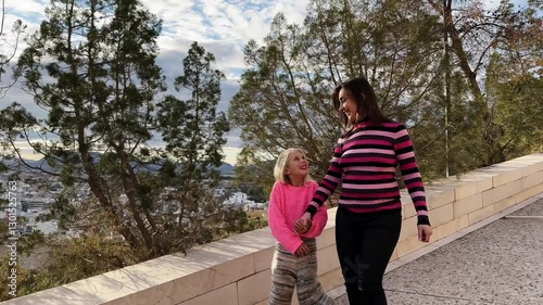 Slow motion video of a mother and daughter enjoying a walk in a park, holding hands and smiling