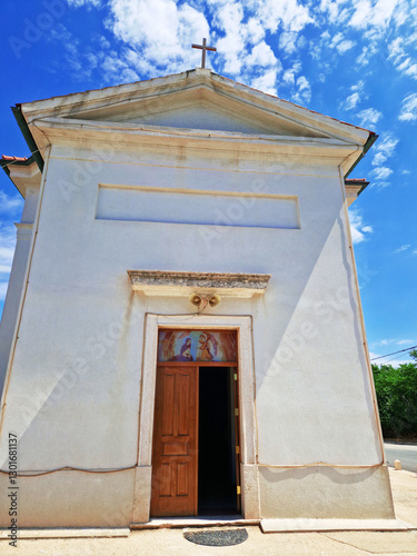 Small white chapel with wooden door under a bright blue sky
