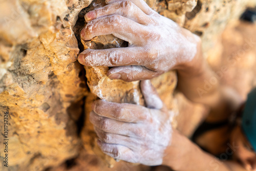 Young girl is engaged in extreme sports, fearlessly climbs up the rock using white magnesia powder, holds her hand to the ledge in the relief,