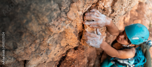 Young girl is engaged in extreme sports, fearlessly climbs up the rock using white magnesia powder, holds her hand to the ledge in the relief,