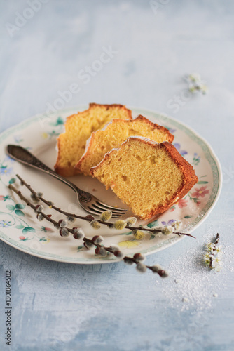 Easter cake sliced ​​of cake on a plate, with a fork and willow branches with catkins, minimalist composition on a muted gray-blue background, close-up.