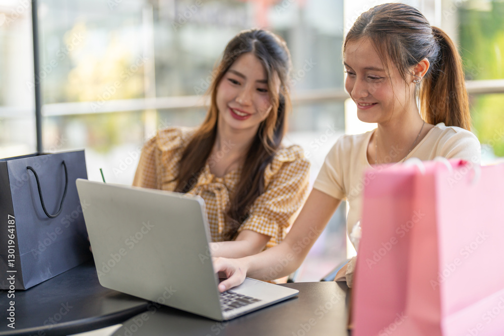 Two diverse women smiling and talking while use laptop for online shopping at cafe, searching for deals and discounts with shopping bags on table, concept of e-commerce, retail, digital lifestyle Two diverse women smiling and talking while use laptop for online shopping at cafe, searching for deals and discounts with shopping bags on table, concept of e-commerce, retail, digital lifestyle
