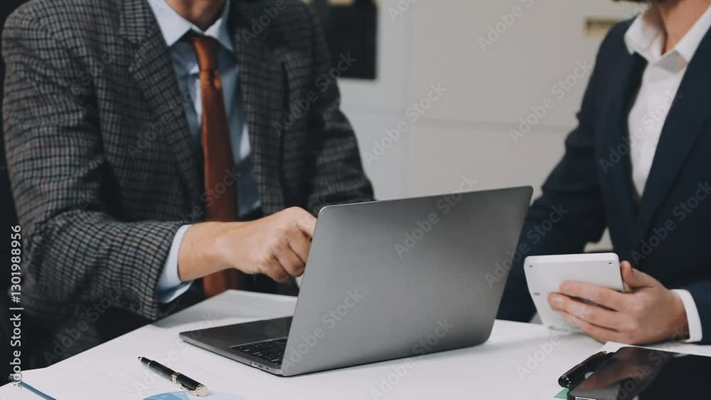 A woman is holding a tablet with a sales report on it. She is talking to another person at a desk A woman is holding a tablet with a sales report on it. She is talking to another person at a desk