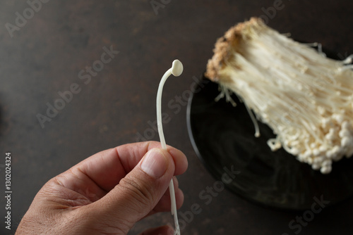 A view of a hand holding a single enoki mushroom. photo