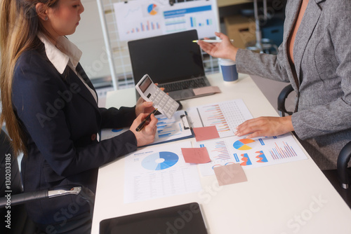 Close-up of two businesswomen working at desk discussing business strategies, analyzing financial charts, planning marketing plans and using laptop to drive business growth in professional office photo