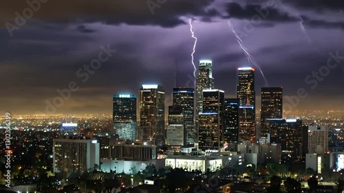 Aerial view of the Los Angeles skyline at night. There are bright skyscrapers in the city and thunder clouds.