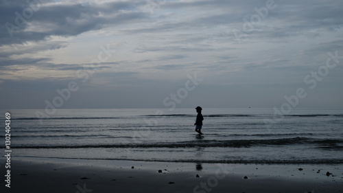 A solitary figure, silhouetted against the soft, muted tones of a twilight seascape, stands at the water's edge.