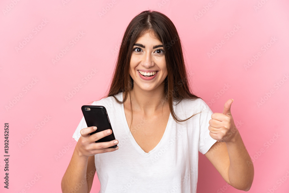 Young caucasian woman isolated on pink background using mobile phone while doing thumbs up Young caucasian woman isolated on pink background using mobile phone while doing thumbs up