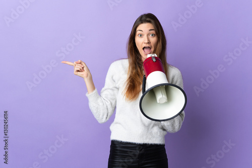 Young Ireland woman isolated on purple background shouting through a megaphone and pointing side