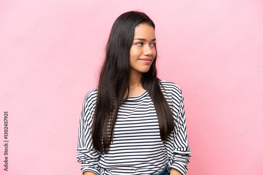 Fototapeta premium Young Colombian woman isolated on pink background having doubts while looking side
