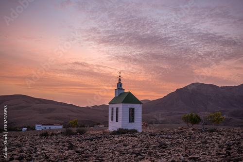 small cute white wooden chapel in a barren volcanic landscape. Sunrise, landscape shot of Ermita Protestante de Violante church, on Fuerteventura island, Canary Islands, Spain 