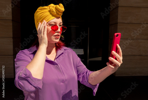 Happy and funny cool lady with fashionable clothes on dark background look to the phone with different emotions - adult asian with extravagant style, concepts about lifestyle, fasion and elderly