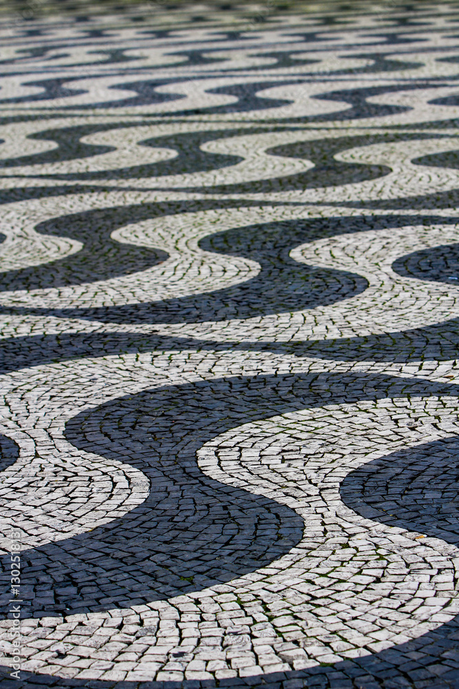Intricate patterns created by cobblestone tiles form a mesmerizing wave design on the pavement of a bustling city square in Lisbon, Portugal Intricate patterns created by cobblestone tiles form a mesmerizing wave design on the pavement of a bustling city square in Lisbon, Portugal