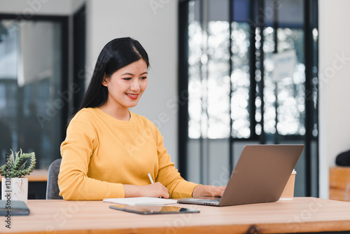 Free Download Confident Asian businesswoman in yellow sweater working on laptop at modern office desk. - GFXLoad