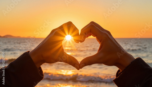 Hands forming heart shape at sunset by the sea. Heart hands with sun flare
