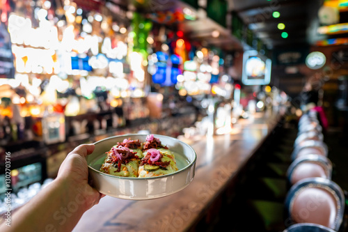 A hand holding a plate of delicious food in a lively bar, with a vibrant and illuminated background showcasing drinks and a bustling atmosphere. photo