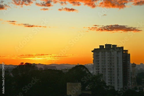 Golden sky in summer sunrise, city buikdings on shadow. Dawn with reddish clouds in the sky. Sun rising over the horizon, yellow reflections in the sky.