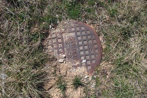 Iron lid for a sanitary sewer with grass and dirt
