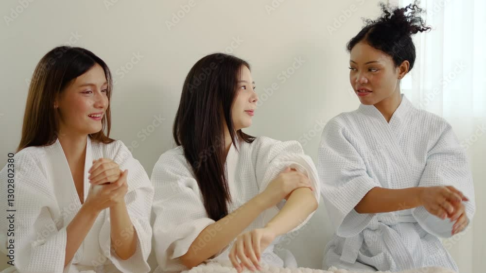 In a cozy bedroom, three young female friends share laughter and joy while applying skin cream on their hands and arms on each other's hands. It's a perfect afternoon of friendship and self-care. In a cozy bedroom, three young female friends share laughter and joy while applying skin cream on their hands and arms on each other's hands. It's a perfect afternoon of friendship and self-care.