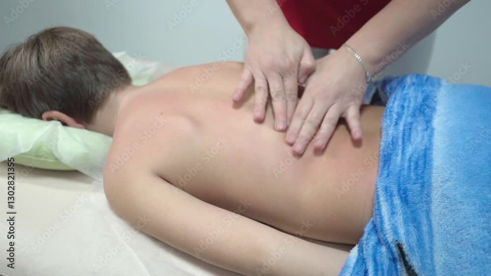 Professional female massage therapist giving back massage to young man in massage booth Professional female massage therapist giving back massage to young man in massage booth