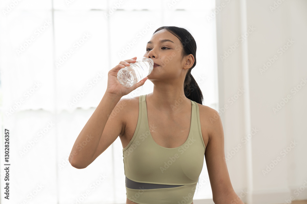 Woman, drinking water. Woman drinking water from bottle during sitting on yoga mat in home. Working out, Exercise, Wearing sportswear, Yoga at home Woman, drinking water. Woman drinking water from bottle during sitting on yoga mat in home. Working out, Exercise, Wearing sportswear, Yoga at home