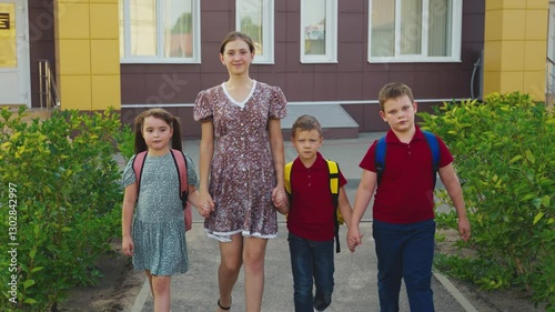 Mother leading children from school, female mother holding children hand, happy family, young nanny with children, schoolchildren with backpacks walking with aunt by the hand, little boys girl walking
