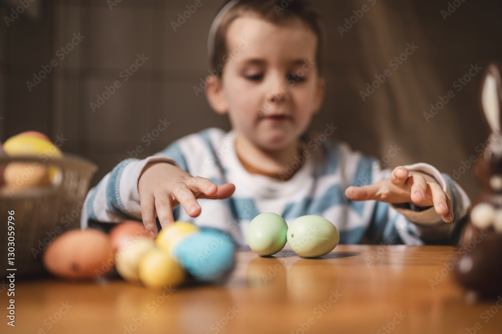 Cute little Boy with bunny ears plays with colored painted eggs, closes eyes with toy, plays hide and seek. Egg hunt, traditional catholic orthodox easter. Little boy celebrate Easter at home Cute little Boy with bunny ears plays with colored painted eggs, closes eyes with toy, plays hide and seek. Egg hunt, traditional catholic orthodox easter. Little boy celebrate Easter at home