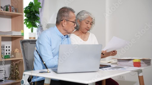 Retired Asian senior couple reviewing and performing financial calculations related to financial documents. Pay taxes online using a laptop