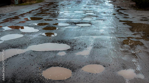 Pits on the road with stones on the asphalt. Destroyed asphalt pavement on the road. Poor road condition requiring repair. View from above. Road construction and repair.