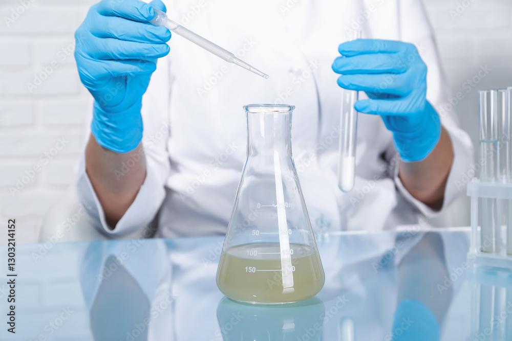 Laboratory testing. Scientist dripping sample from pipette into flask at table indoors, closeup Laboratory testing. Scientist dripping sample from pipette into flask at table indoors, closeup