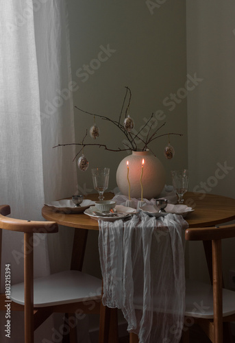 Festive Easter setting - easter bouquet in a ceramic vase, dishes, burning candles on a round wooden table in the living room