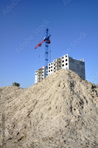 A pile of construction sand in front of buildings under construction. construction crane. vertical image