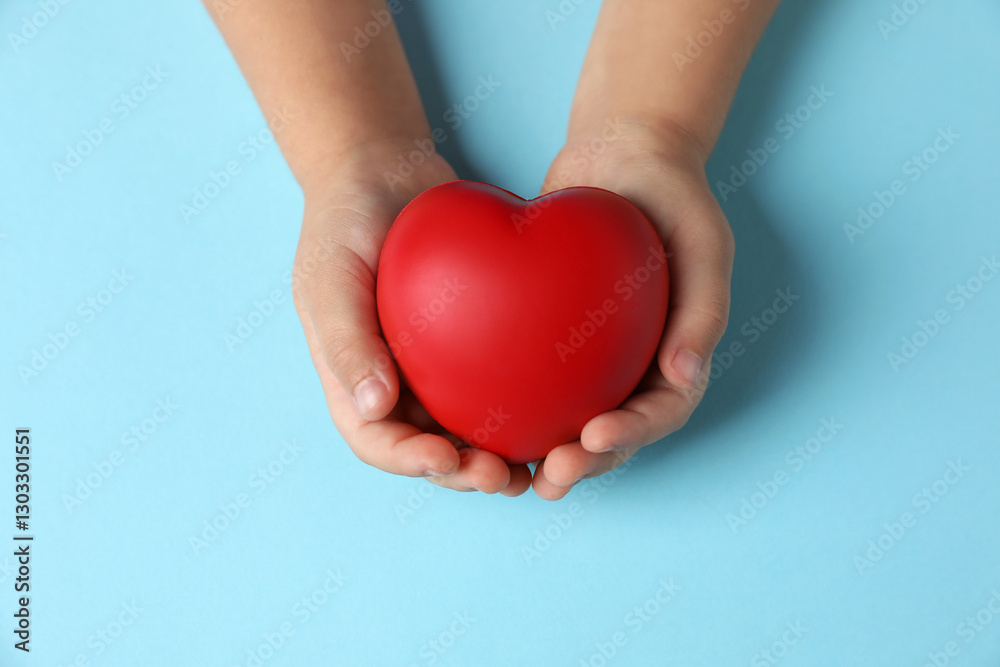 Child holding decorative red heart on light blue background, top view Child holding decorative red heart on light blue background, top view